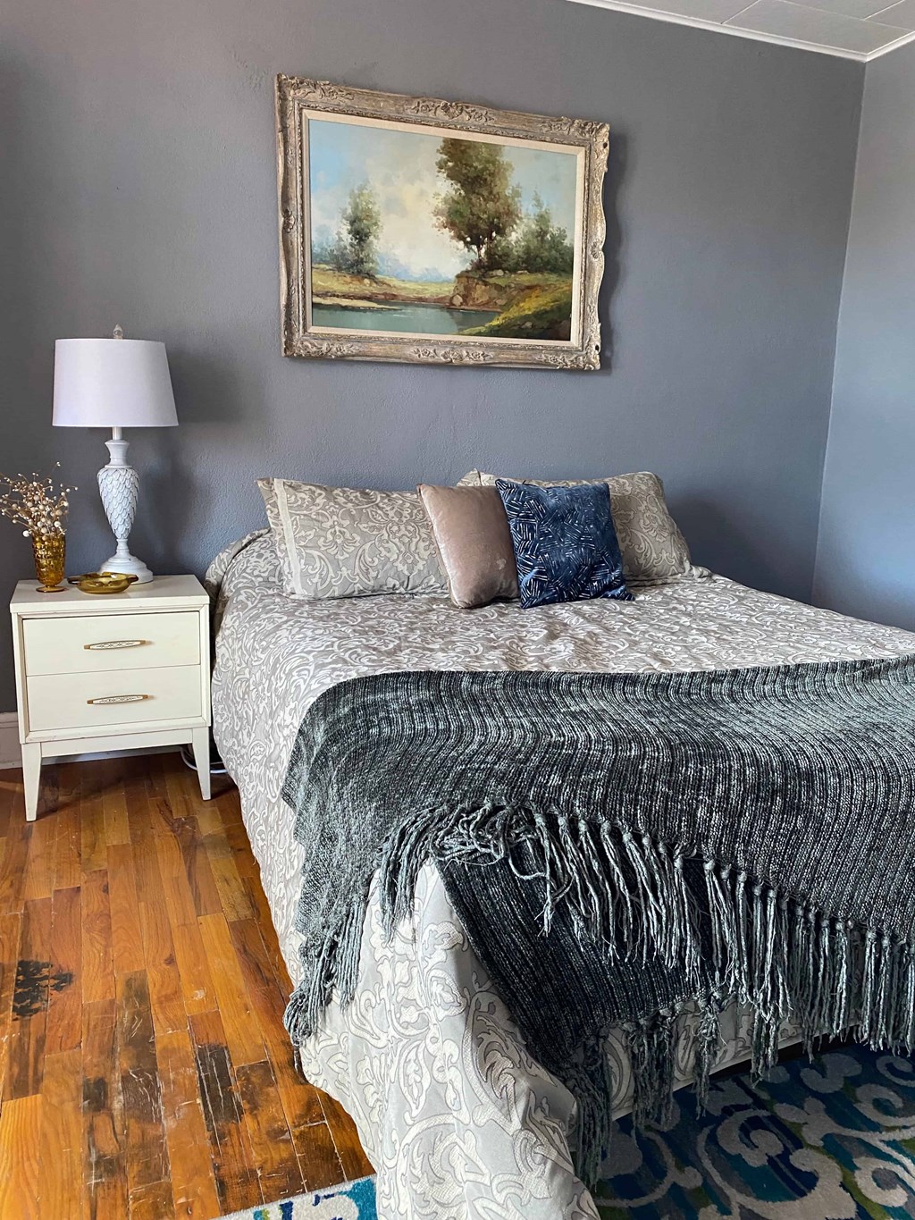 A bedroom with a bed, a nightstand, and a painting on the wall.