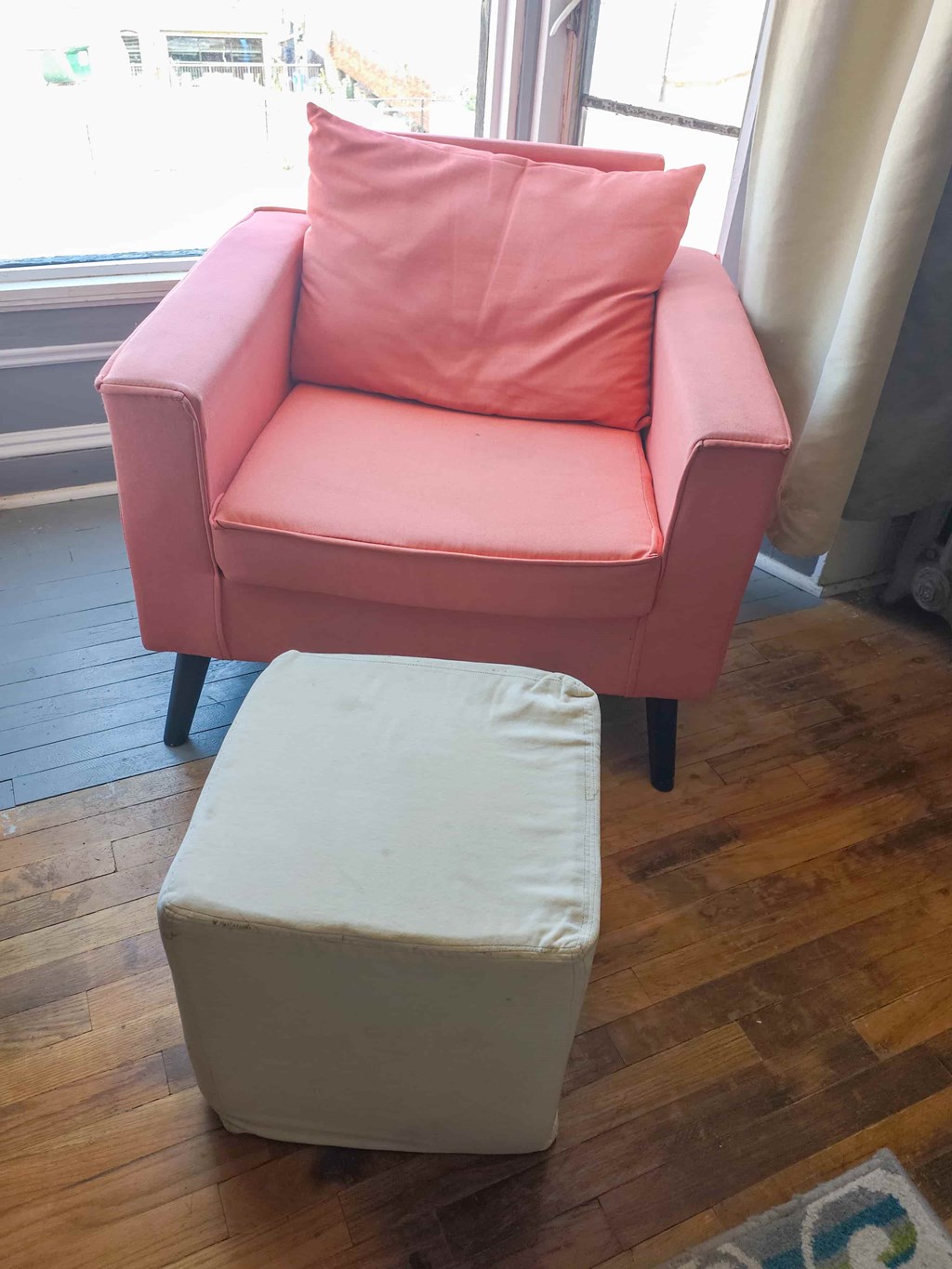 A pink chair with a pink pillow and a white ottoman.