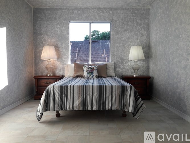 A bedroom with a bed, two lamps, and a window.