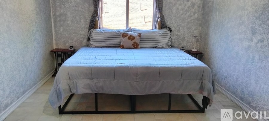 A bed with a blue comforter and two pillows sits in a room with a window.