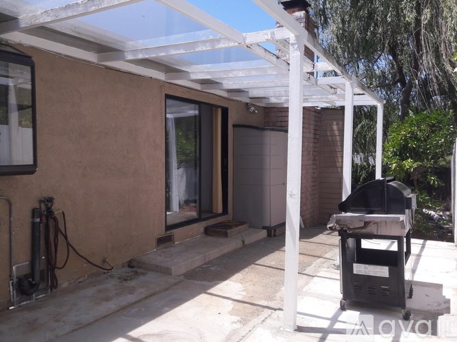 A patio with a white pergola and a black trash bin.