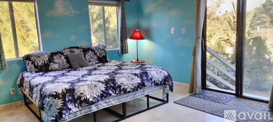 A bed with a blue and white comforter sits in a room with a red lamp.