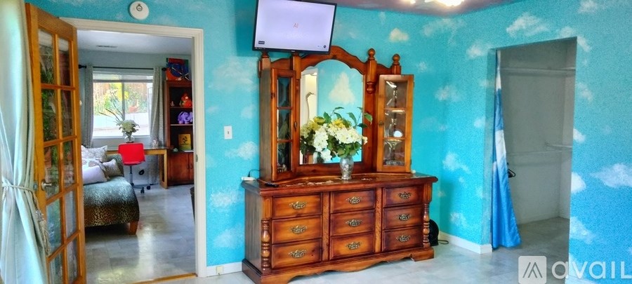 A bedroom with a blue wall and a wooden dresser with a mirror on top.