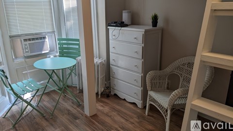 A room with a white dresser, a green chair, and a white chair.