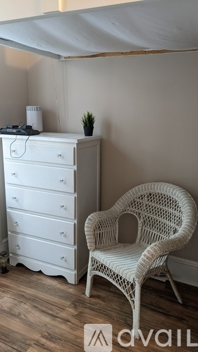 A white chair sits in front of a white dresser in a room with wooden floors.