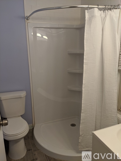 A white toilet sits next to a white shower curtain in a bathroom.