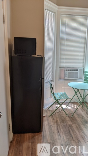 A black refrigerator stands in a kitchen next to a table with a green chair.