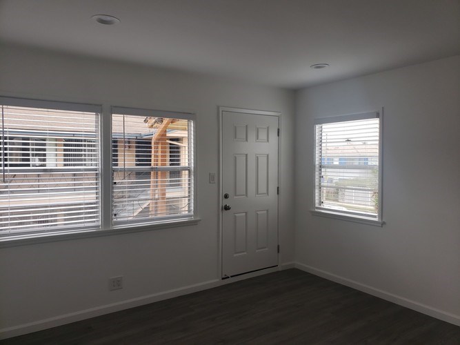 A room with a white door, a window with blinds, and a window without blinds.