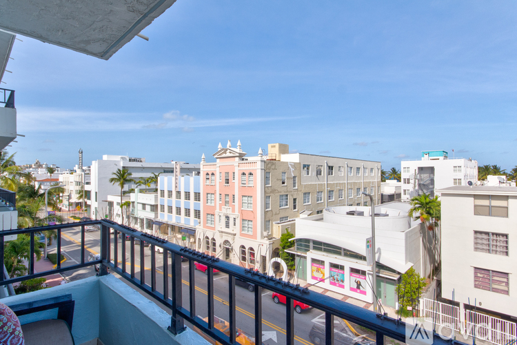 A balcony overlooks a city street with buildings and a clear blue sky.