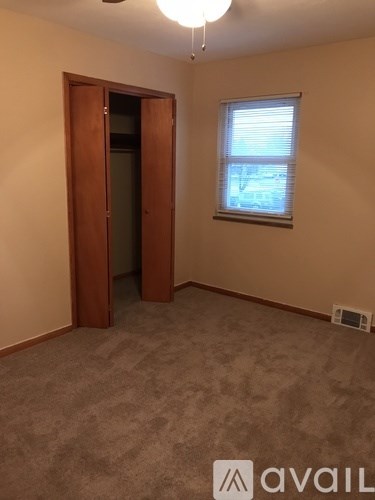 A room with a carpeted floor, a window with blinds, a ceiling fan, and a wooden door.