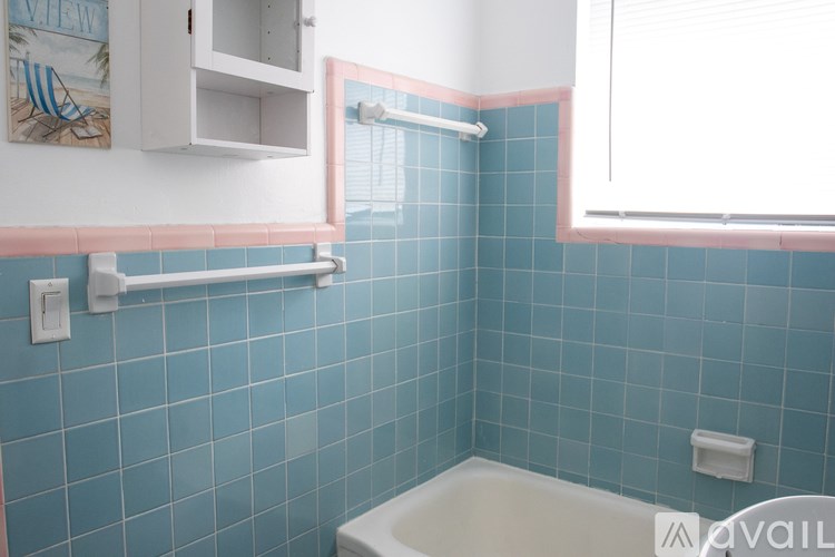 A blue tiled bathroom with a white tub and a window.