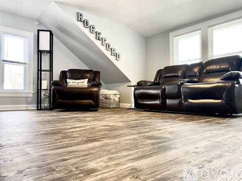 A living room with a black leather sofa and chair with a white cushion and a sign on the wall.
