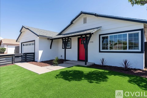 A white house with a red door and a black awning is for sale.