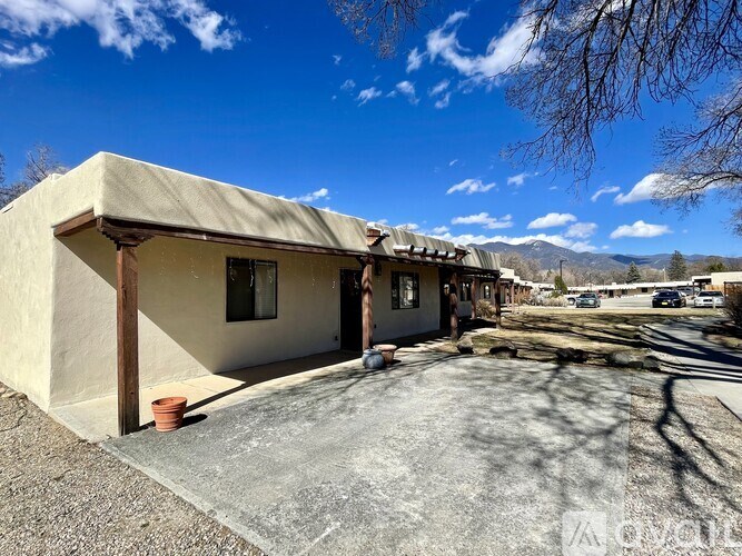 A house with a beige exterior and a brown roof is shown with a clear blue sky above.