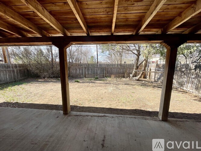 A wooden covered patio with a view of a fence and trees.
