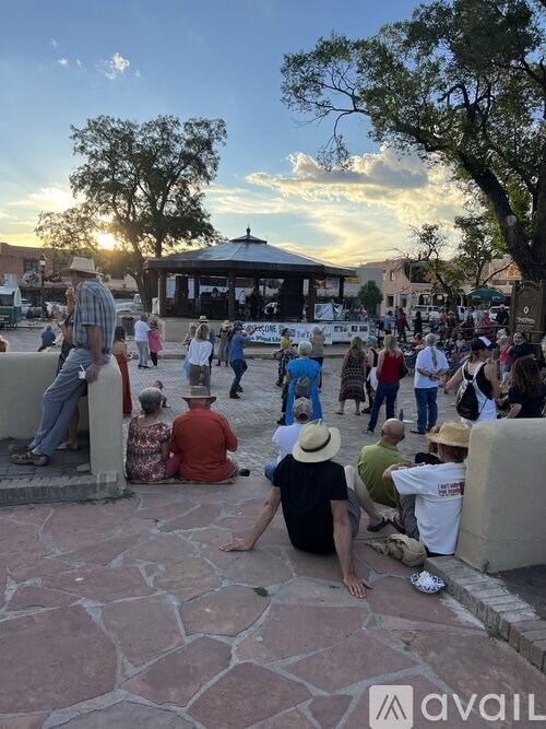 A group of people are sitting and standing on a stone walkway in a park.