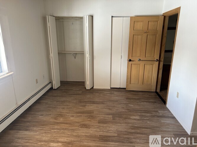 A room with a wooden floor and a white wall with a door and a wardrobe.