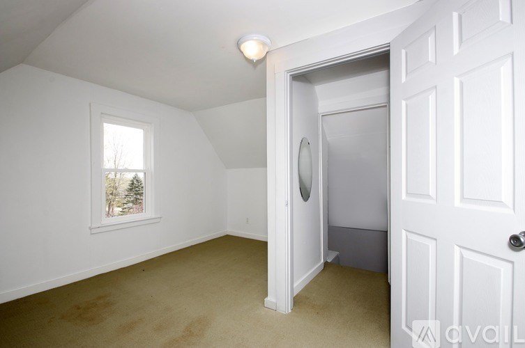 A room with a white door and a window with a view of trees.