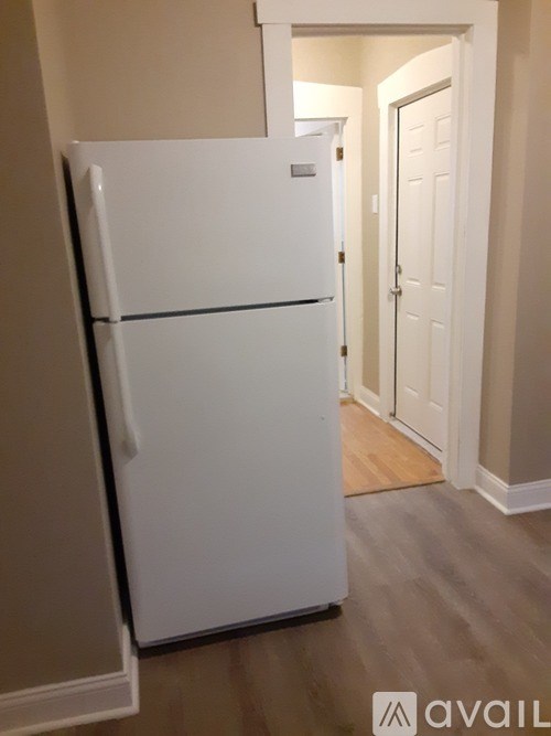 A white refrigerator in a room with a wooden floor.