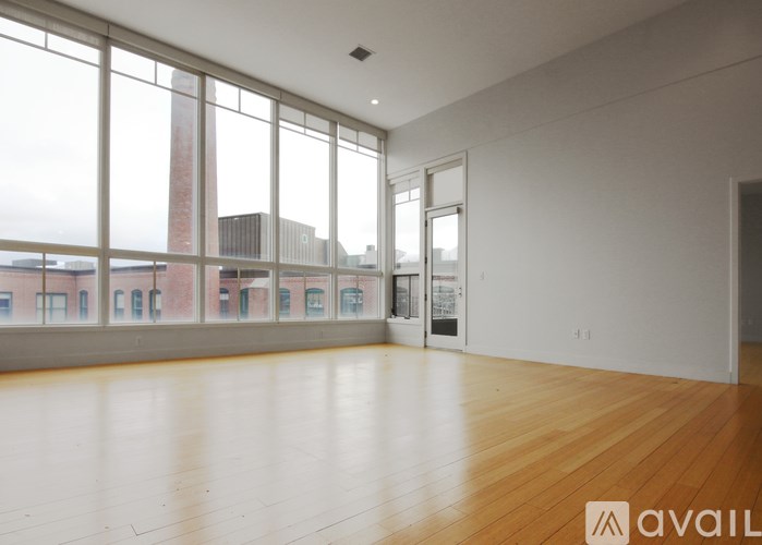 A large empty room with wooden floors and a view of a cityscape through the windows.