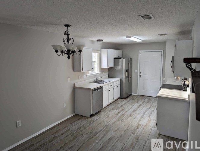 A kitchen with white appliances and cabinets, a chandelier, and a wooden floor.