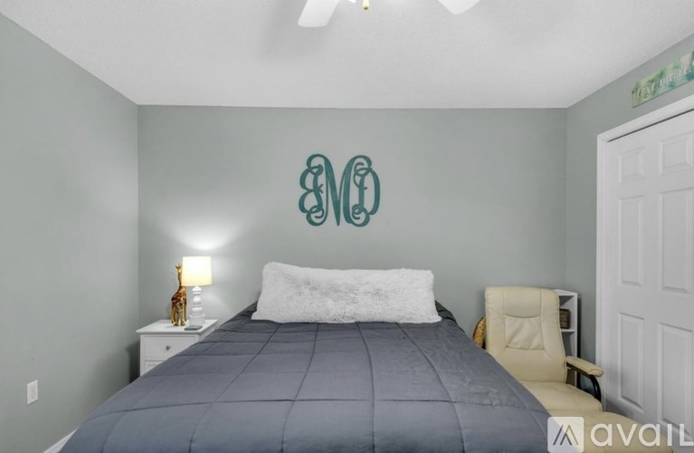 A bedroom with a bed, chair, and a monogrammed wall.