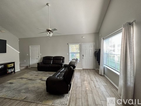 A living room with a black leather couch and a ceiling fan.