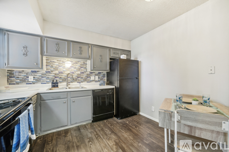 A kitchen with a black refrigerator and wooden floors.