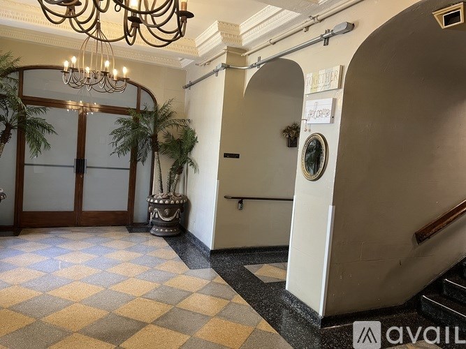 A hallway with a chandelier, a plant, and a checkered floor.