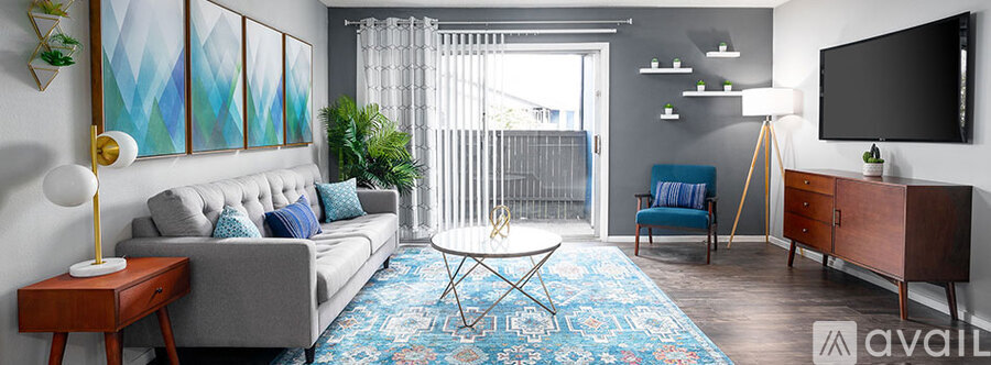 A living room with a grey couch, a blue chair, a wooden side table, a rug, and a television.