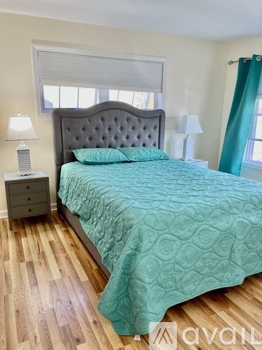 A bed with a grey headboard and a teal comforter in a room with wooden flooring.