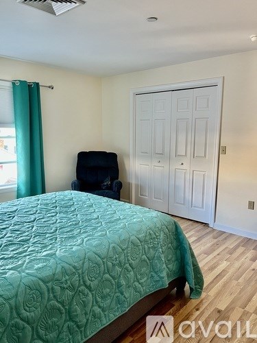 A bedroom with a bed, chair, and a door.