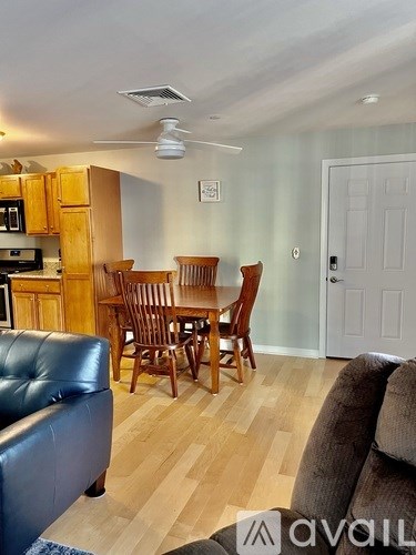A living room with a black leather couch and wooden chairs.
