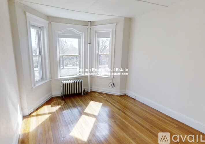 A room with wooden floors and white walls, with a window and a radiator.