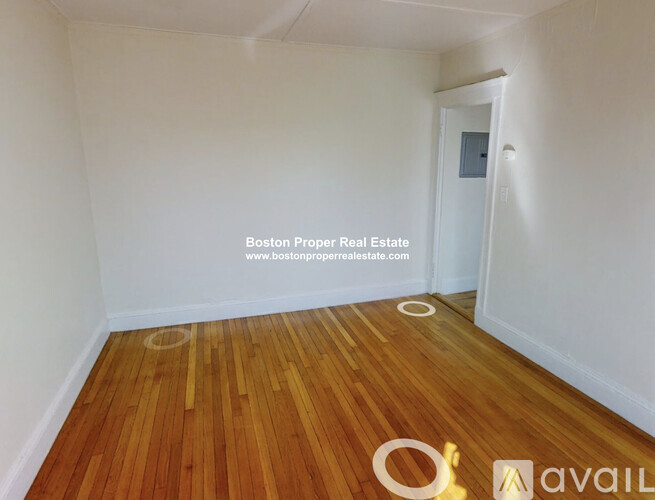 A room with wooden flooring and white walls, with a doorway leading to another room.