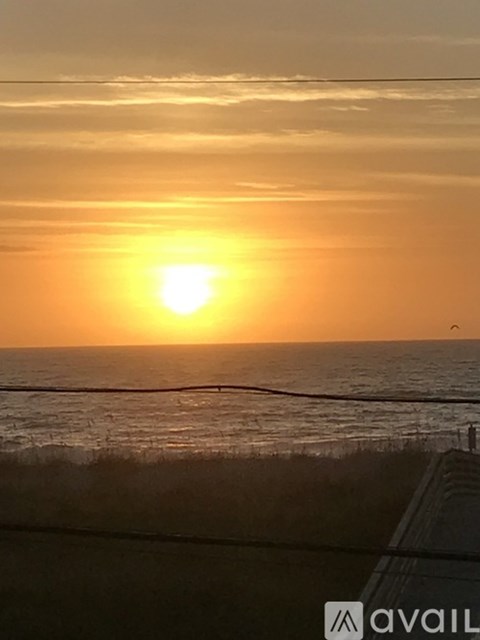 The sun is setting over the ocean with a road in the foreground.