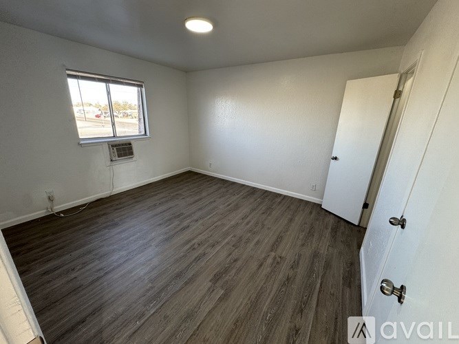A room with wooden flooring and a window with a view of a parking lot.