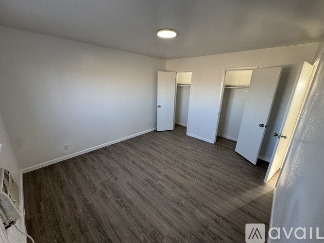 A room with wooden flooring and white walls, with a few doors visible.