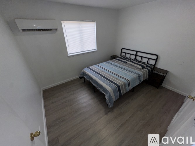 A bedroom with a bed, wooden flooring, and a window with blinds.