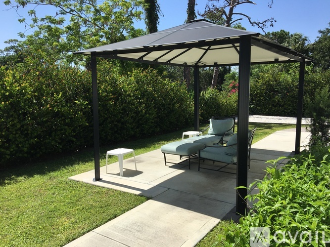 A black and white gazebo with a table and chairs is surrounded by greenery.