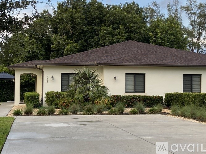 A house with a brown roof and a white exterior is surrounded by greenery.