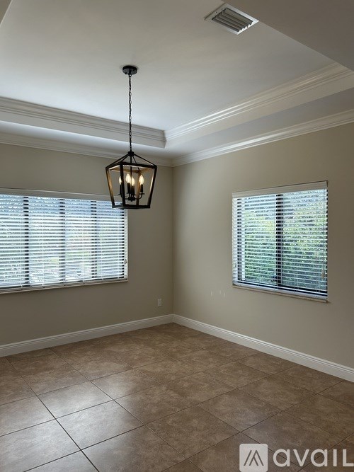 A room with a light hanging from the ceiling and two windows with blinds.