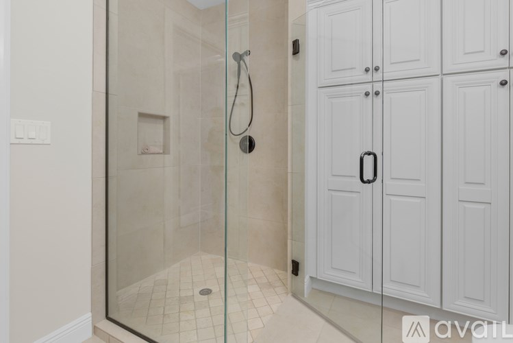 A bathroom with a glass shower door and white cabinets.