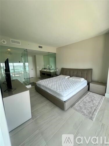 A bedroom with a large bed, a television, and a glass wall.