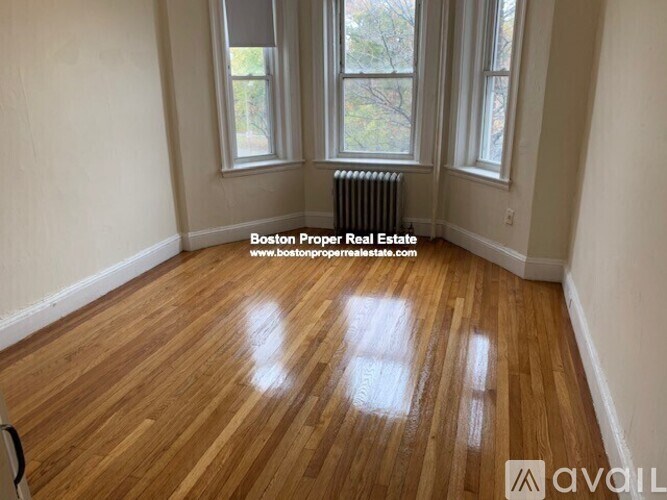 A room with wooden flooring and a window overlooking a tree-filled yard.