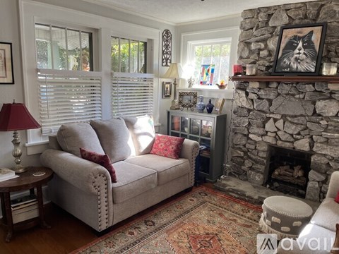 A living room with a grey couch, a stone fireplace, and a painting of a cat on the wall.