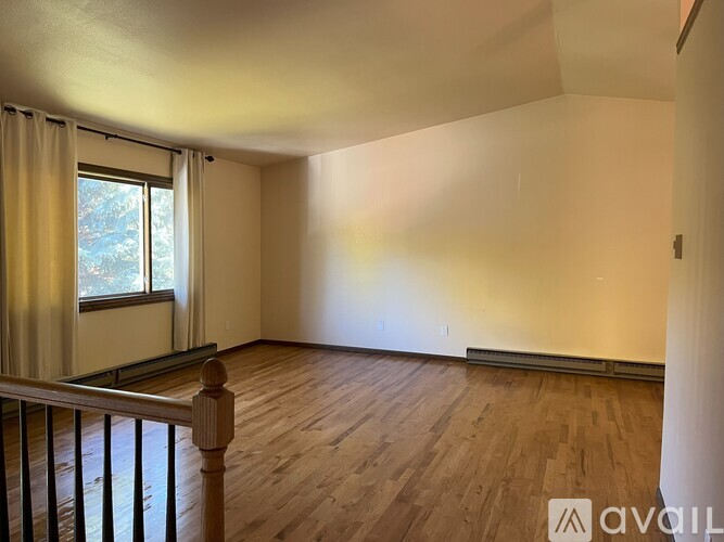 A room with wooden floors and a window with curtains.