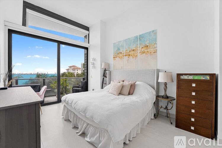 A bedroom with a large bed and a view of the ocean through a sliding glass door.