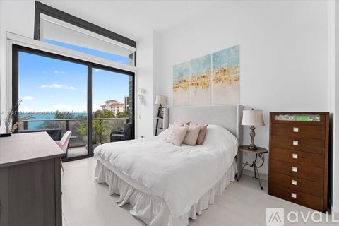 A bedroom with a large bed and a view of the ocean through a sliding glass door.