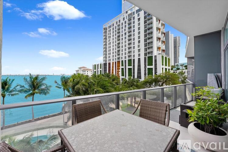 A balcony with a table and chairs overlooks a pool and a view of the ocean.